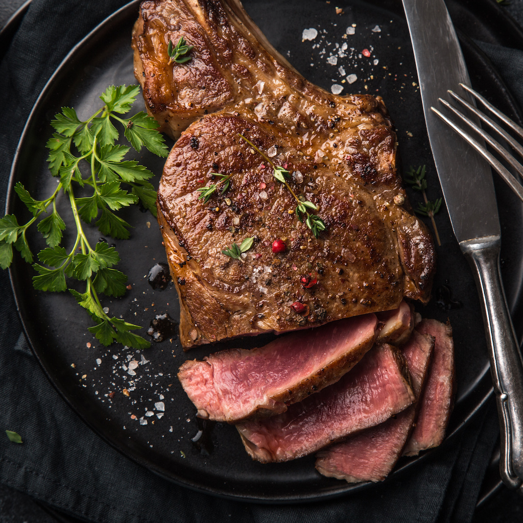 sliced beef steak on black plate, dark background, top view